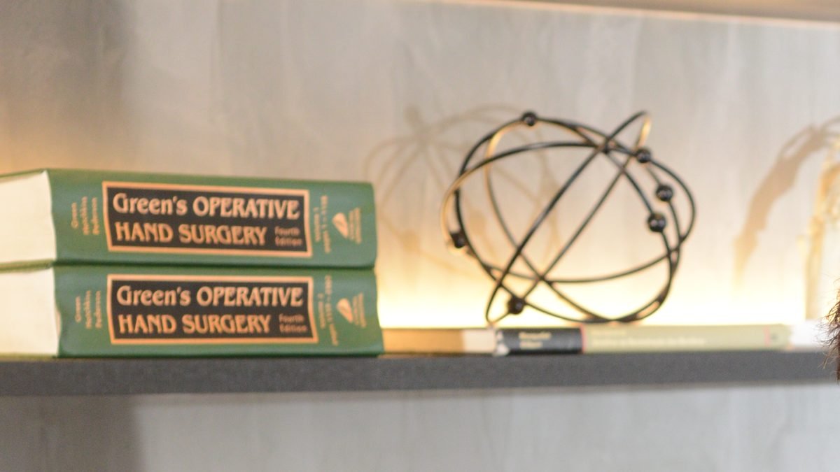 Estante do consultório com os volumes do Green's Operative Hand Surgery